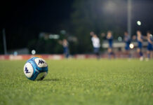 How to Handicap Soccer Odds Without Offshore Risk A soccer ball on a grass pitch at night, with players and floodlights blurred in the background